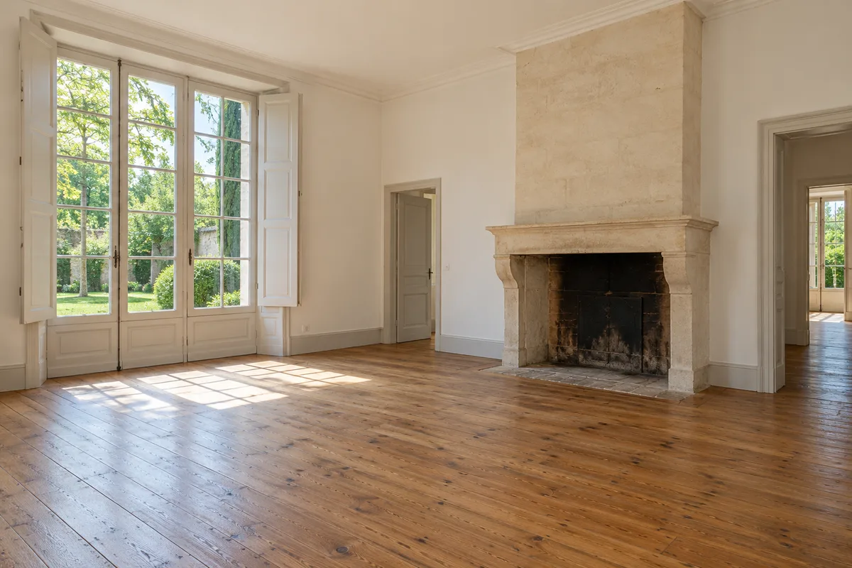 Salon vide d&rsquo;une maison ancienne avec parquet et volets ouverts sur le jardin